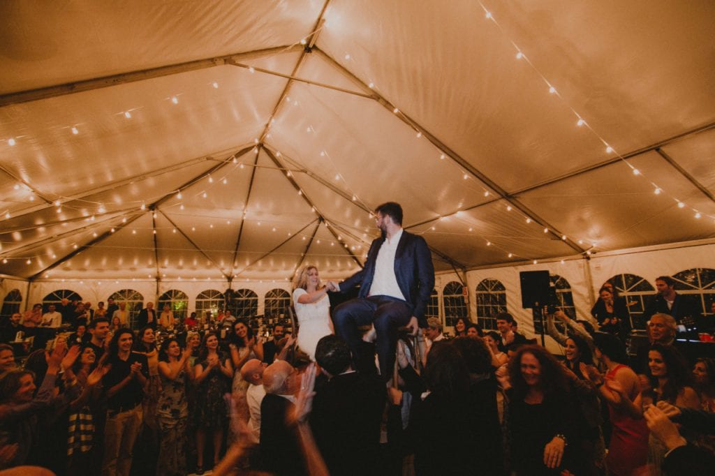 bride and groom up on chairs in dancing crowd
