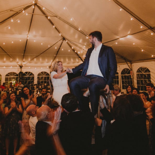 bride and groom up on chairs in dancing crowd